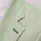 Close-up of a light sage green herringbone fabric with a small dark green embroidered accent on a jacket or garment.