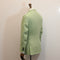 A light sage green linen blazer shown from the back on a wooden dress form mannequin against a plain off-white wall.