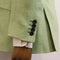 Close-up of a light sage green herringbone blazer sleeve with four dark buttons, shown on a wooden mannequin arm with a striped dress shirt cuff visible.