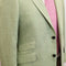 A close-up of a light sage green linen blazer with a pink tie underneath, featuring a two-button closure and flap pockets.
